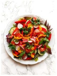En un plato de porcelana se ve una ensalada compuesta por hojas de rúcula  y mostaza, rabanitos, pimientos de colores y pepino. Se trata de una ensalada rica en glucosinolatos destinada a mejorar la salud física y mental