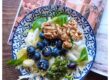 Plato de ensalada fresca con endivias, canónigos, arándanos, nueces y garbanzos sobre una mesa de madera, acompañado de una revista de viajes y luz natural. Ambiente tranquilo, sin dispositivos electrónicos a la vista.